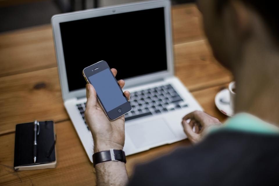 Hands holding a phone over a laptop