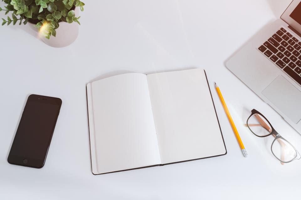 Notebook, phone and glasses on a white desk