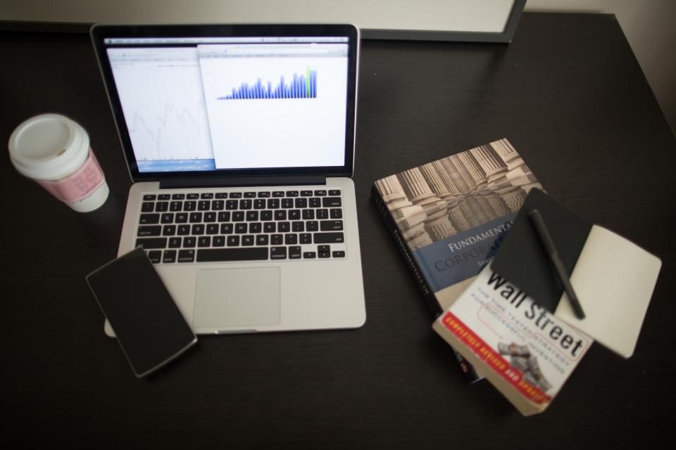 Laptop showing a chart beside a notebook and phone