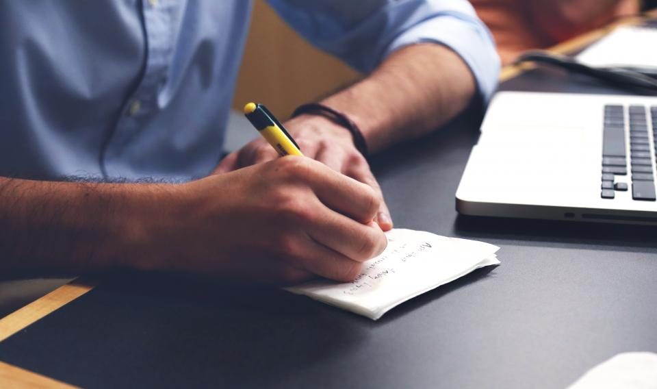 Man writing notes at a desk beside a laptop