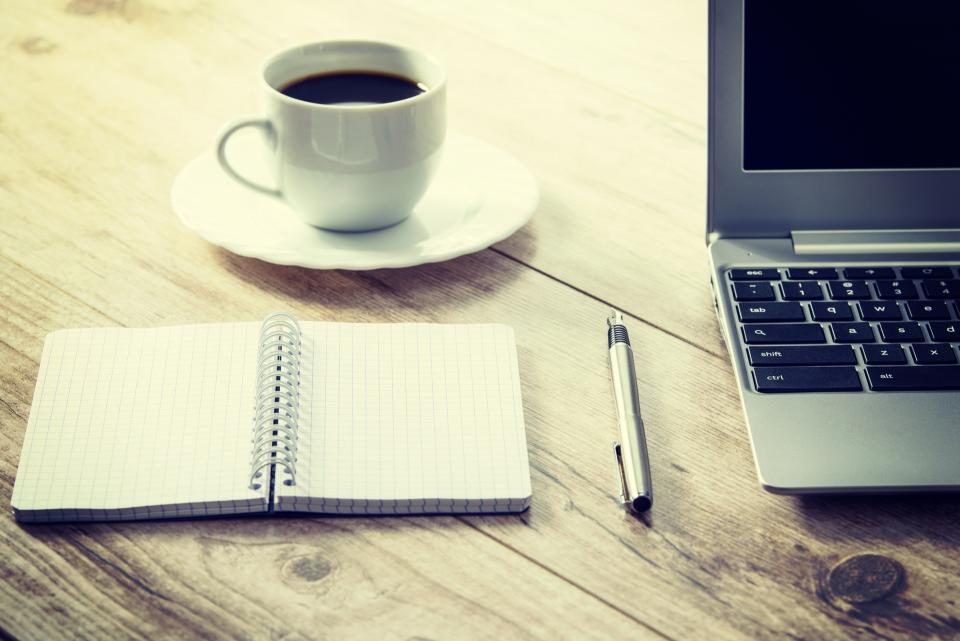 Notebook, coffee cup and laptop on a wooden desk