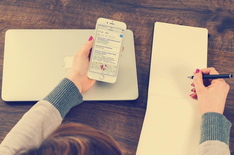 Hands holding a phone and writing in a notebook