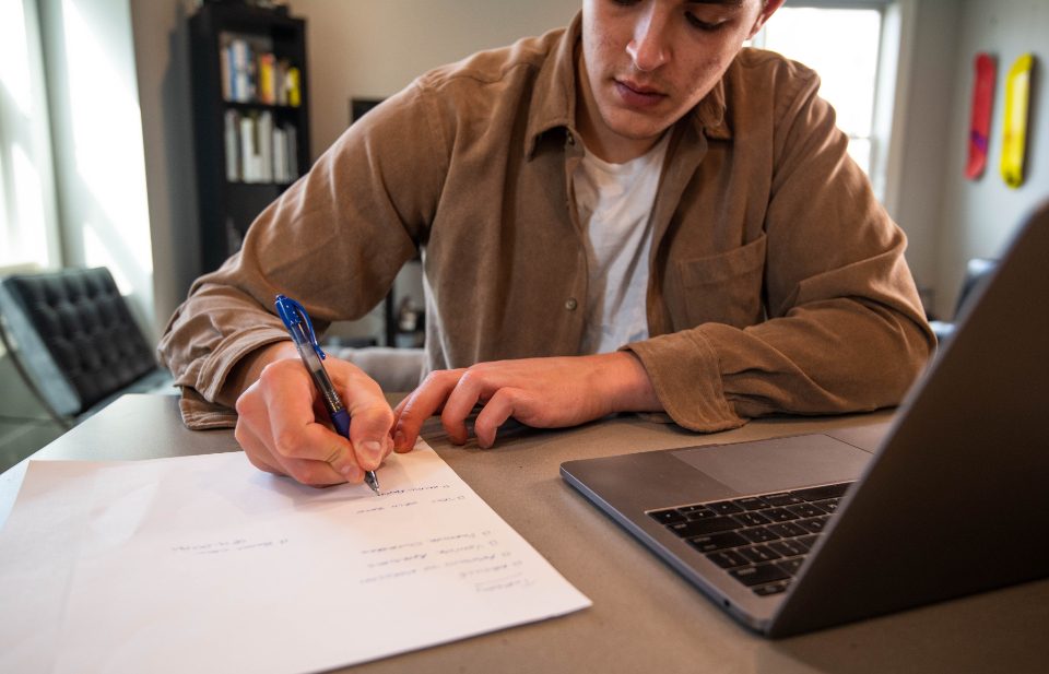 Young man writing notes beside a laptop