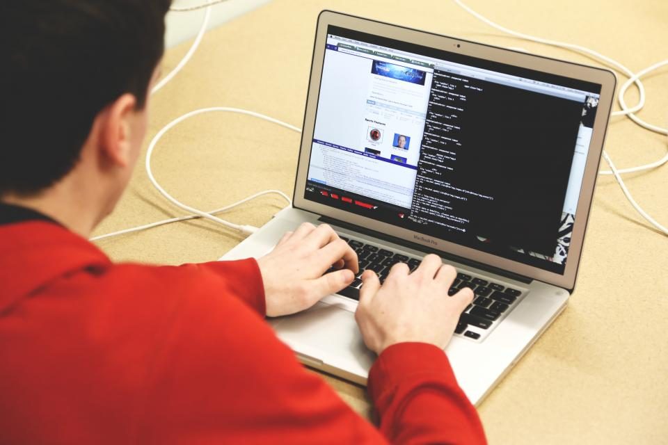 Man in a red jumper typing on a laptop