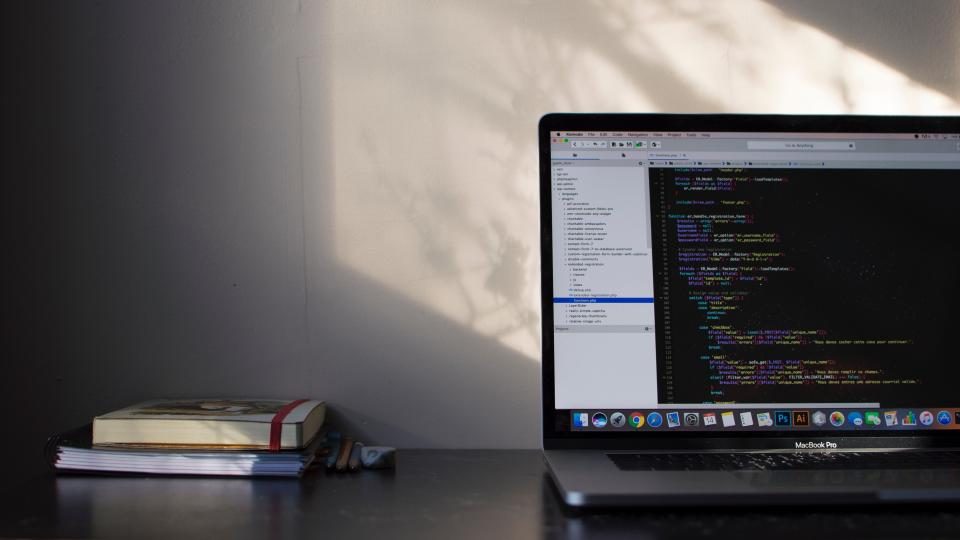 Laptop showing code on a desk beside books