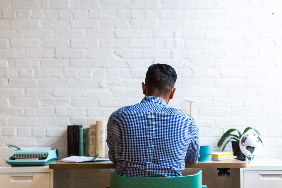 Man working at a desk against a white brick wall