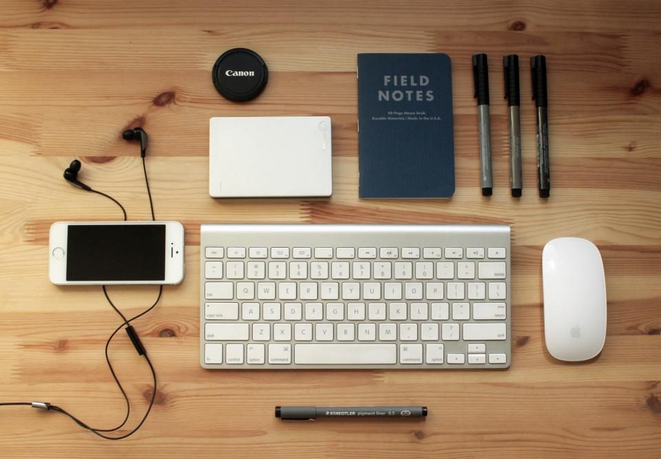 Keyboard, phone, notebooks and pens on a wooden desk
