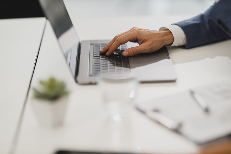 Hand on a laptop at a bright desk