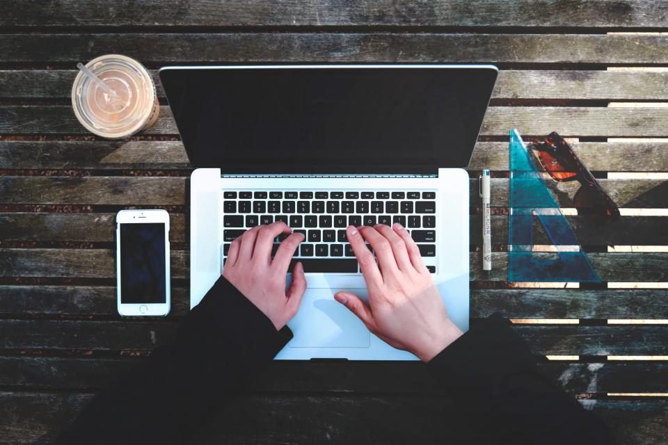 Hands typing on a laptop on a wooden table