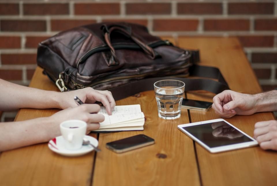 Two people at a table with coffee, notes and a tablet