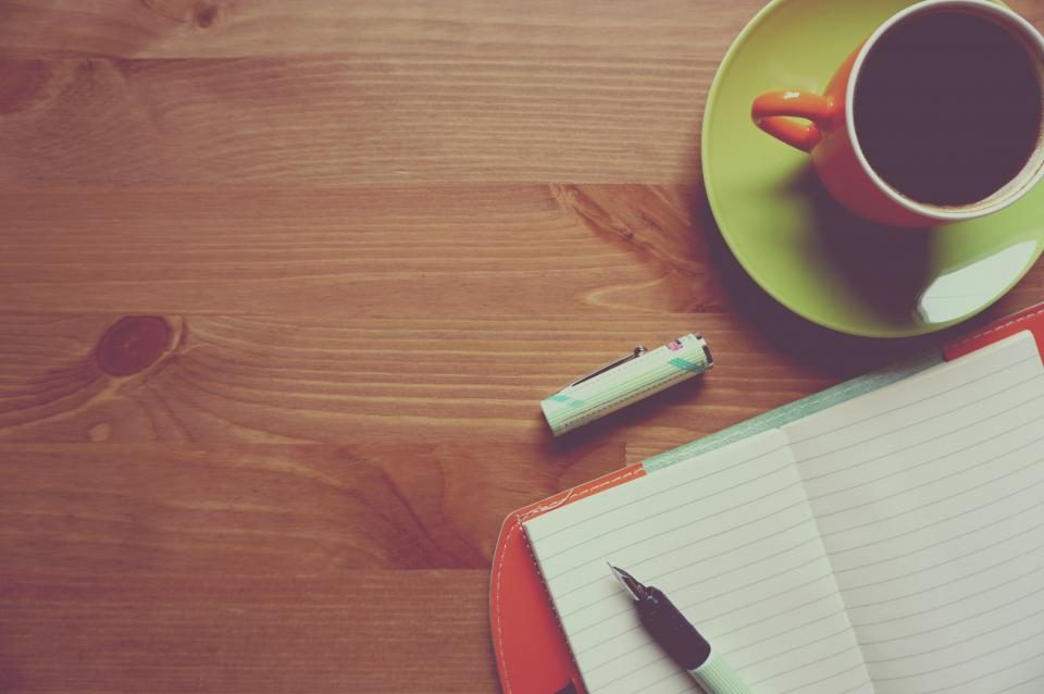 Coffee cup, notebook and pen on a wooden table