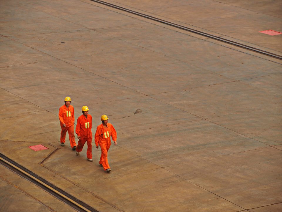 Three workers in hard hats and orange overalls walking