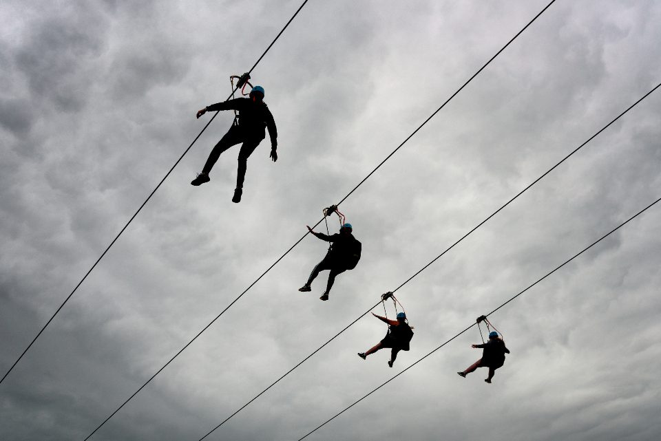 People zip-lining against a cloudy sky