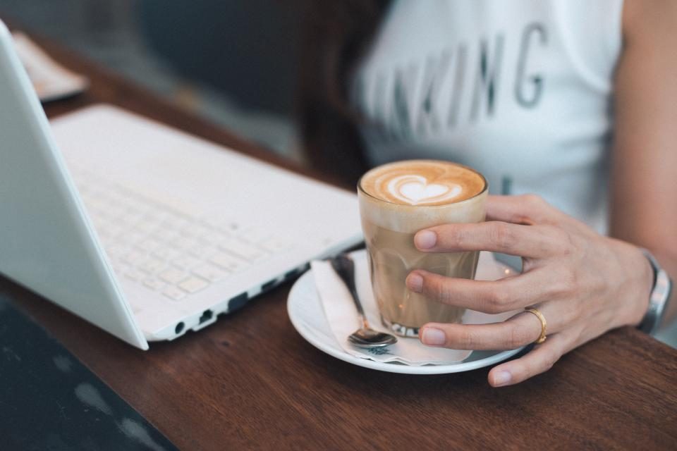 Hands holding a coffee beside a laptop