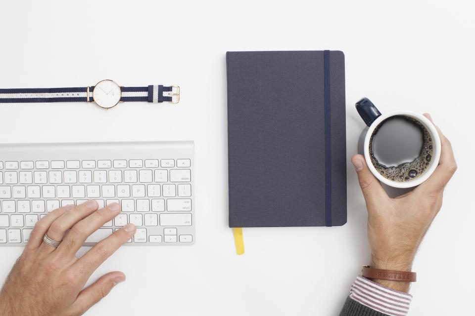 Keyboard, watch, notebook and coffee on a white desk