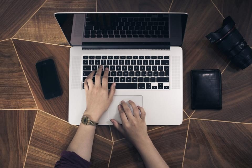 Hands typing on a laptop on a wooden desk